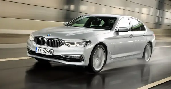 Srebrne BMW 520d xDrive w ruchu, z rozpryskującą się wodą spod kół, w nowoczesnym tunelu.