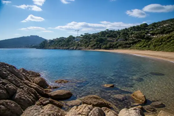 Baia tranquilla con acque cristalline e sabbia dorata, una delle splendide porto ercole spiagge, incorniciata da rocce e vegetazione lussureggiante.