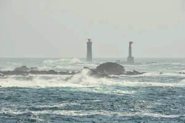Deux phares se dressent sur des îlots rocheux battus par les vagues, au large de l'île d'Ouessant.