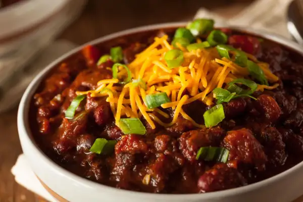 Gęste, aromatyczne chili con carne w białej misce, posypane startym serem i szczypiorkiem. Idealne na chłodne wieczory.