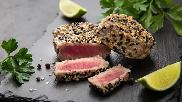 Apetyczny stek z tuńczyka w sezamie, idealnie wysmażony, z kawałkami limonki i natką pietruszki.