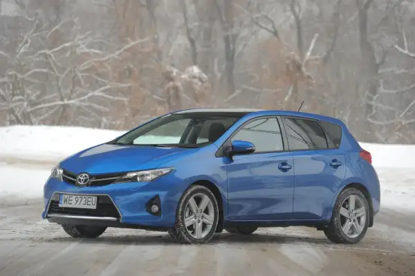 Niebieski Toyota Auris na śniegu, z widocznymi przednimi żarówkami.
