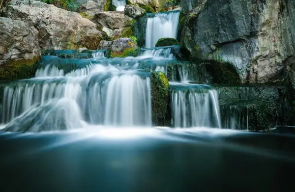 Serene waterfall photography captures cascading water flowing over moss-covered rocks, creating a tranquil, misty scene.