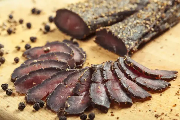 Tranches de filet mignon séché, assaisonnées de poivre noir, disposées sur une planche en bois.