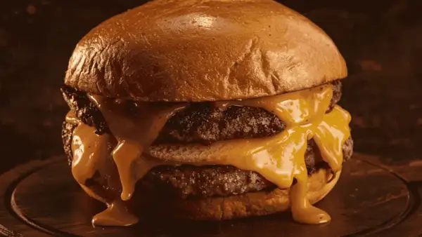 Gros plan sur un burger double au fromage fondant dégoulinant, sur un pain brioché doré.