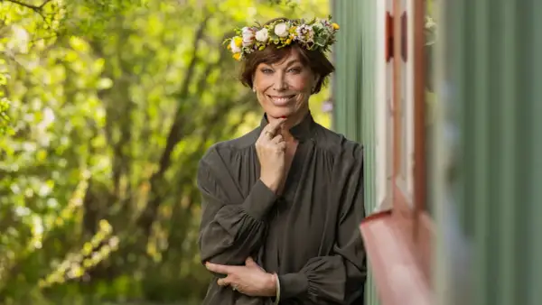 En kvinna med blomsterkrans ler mot kameran. Hon påminner om en sommarbild av mischa billing familj.
