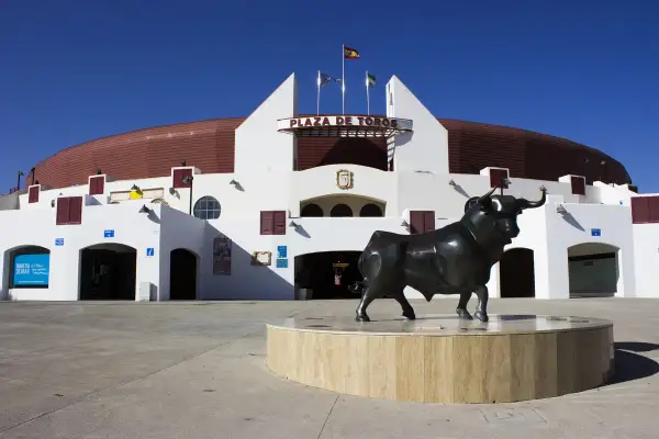 Escultura de toro frente a la Plaza de Toros Roquetas de Mar, bajo un cielo azul intenso.
