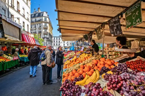 Frukt och grönsaksstånd på en livlig loppmarknad i Paris. Folk handlar bland färska druvor, apelsiner och tomater.