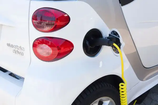 Biały samochód elektryczny z podłączonym żółtym kablem do ładowania.