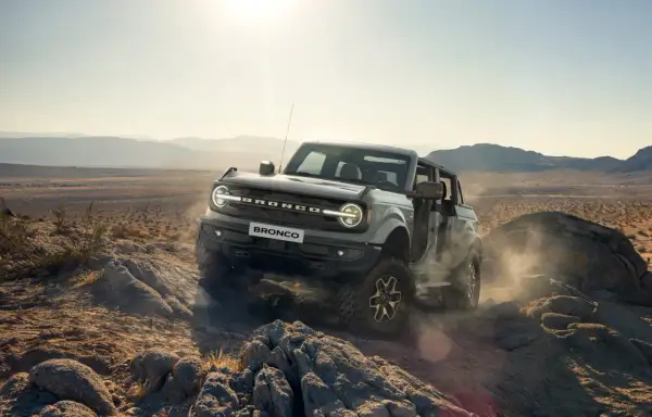 Ford Bronco pokonuje skalisty teren pustyni, wzbijając tumany kurzu.