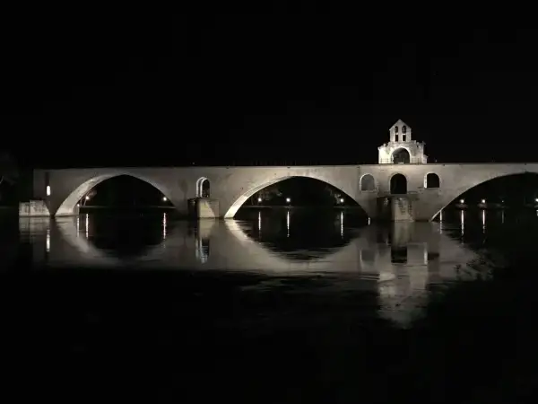 Nocna panorama na moście w Avignon. Kamienne łuki odbijają się w spokojnej wodzie rzeki Rodan.
