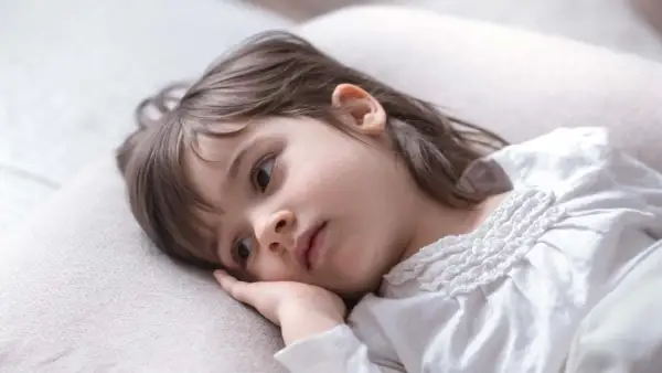 Smutna dziewczynka leży na poduszce, zamyślona. Może to oznaka problemów z zasypianiem u dziecka 7-letniego.