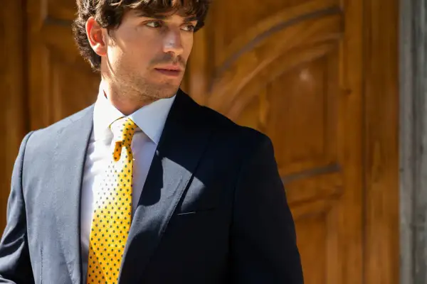 Uomo elegante con giacca blu, camicia bianca e cravatta gialla con pois, annodata con un perfetto nodo Windsor.