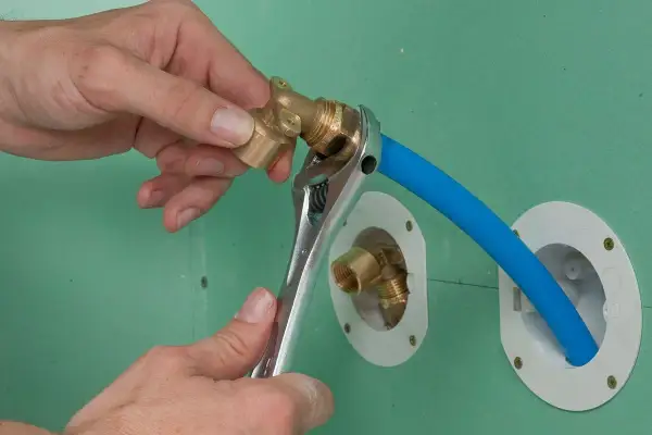 Installation d'un raccord pour l'arrivée d'eau de la douche. Une clé serre un coude en laiton sur un tuyau bleu.