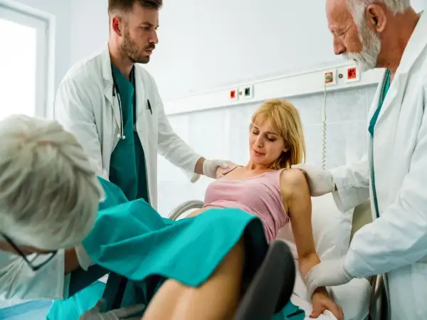 Kobieta w szpitalu, otoczona przez lekarzy, przechodzi przez poród.
