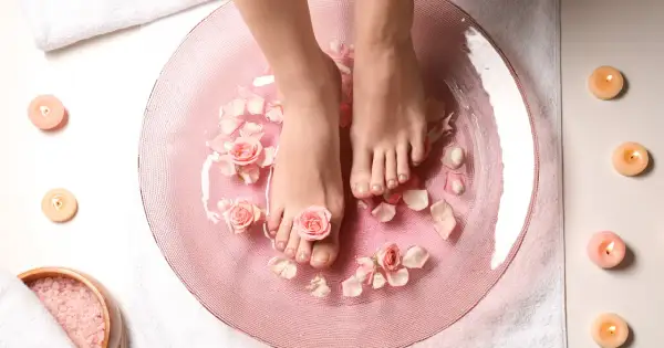 Relaks w domowym spa: stopy w różowej kąpieli z płatkami róż i świecami. To właśnie jest pedicure co to znaczy – dbanie o stopy.