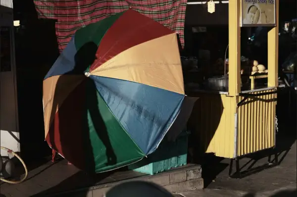 Kolorowy parasol rzuca cień na uliczny stragan z mango sticky rice. Tętniący życiem krajobraz miejski.