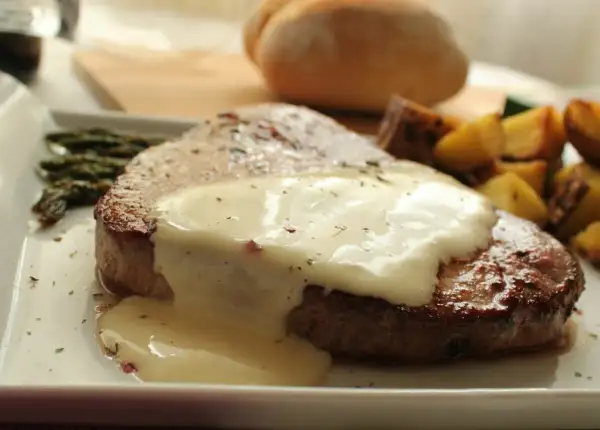 Filete redondo cubierto con una cremosa salsa blanca, acompañado de espárragos y patatas asadas.
