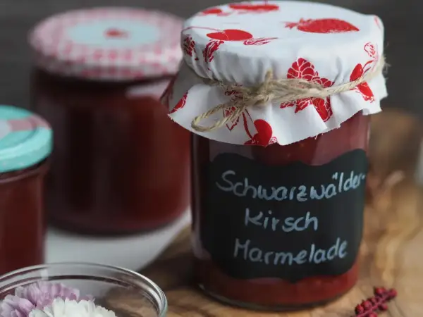 Glas mit hausgemachter Kirschmarmelade, beschriftet mit "Schwarzwälder Kirsch Marmelade". Ein tolles Rezept für den Sommer!