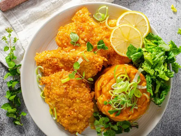 Knuspriges Zucchin Schnitzel mit Kürbispüree, Salat und Zitronenspalten.