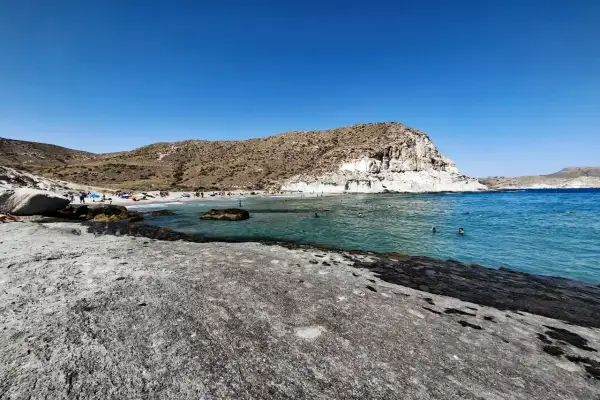 Gente disfrutando del sol y el mar en la cala de enmedio almeria, con aguas cristalinas y formaciones rocosas.