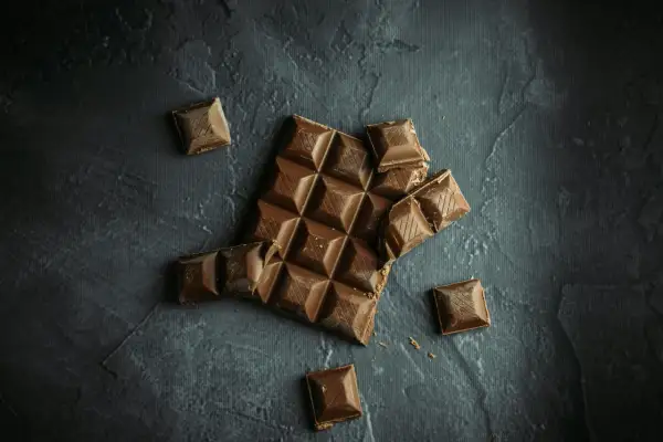 Tableta de chocolate rota y trozos sueltos sobre fondo oscuro. ¡Sí, puedo llevar chocolates en la maleta de mano!