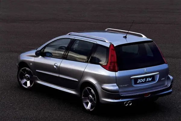 Srebrny Peugeot 206 SW z relingami dachowymi i podwójnym wydechem, zaparkowany na ciemnym asfalcie.