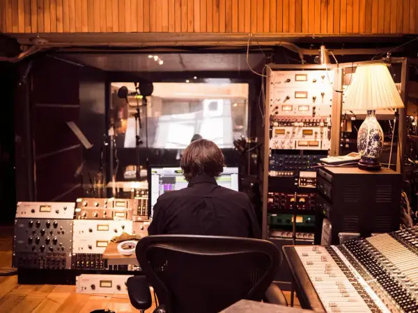 Producent muzyczny w studio, otoczony sprzętem, tworzy nową muzykę, być może z pomocą sztucznej inteligencji.