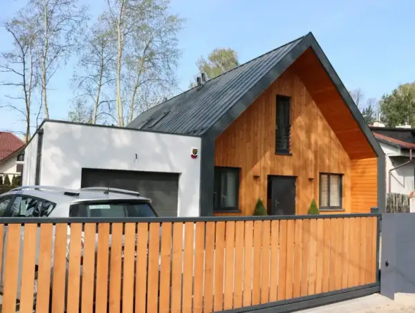 Nowoczesny dom z murowaną częścią i garażem, do którego przylega dobudówka drewniana.