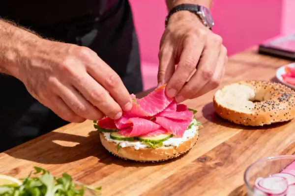Préparation d'un bagel garni de saumon fumé, de fromage frais et de concombre. Un accompagnement bagel parfait pour un brunch.