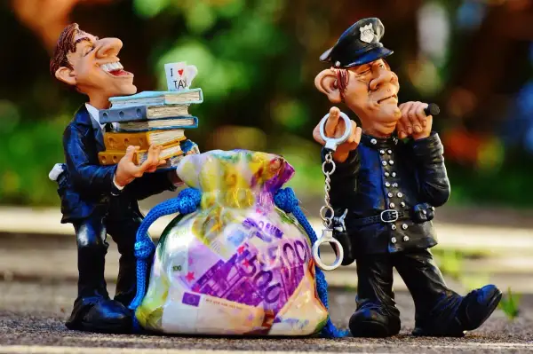 Figurki: uradowany mężczyzna z książkami i kubkiem "I LOVE TAX" obok policjanta z kajdankami i torbą pieniędzy. To poświadczenie nieprawdy przykłady.