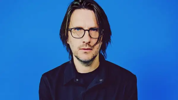 Steven Wilson, lider zespołu Porcupine Tree, w okularach i czarnej koszuli na niebieskim tle.