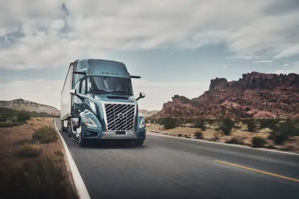 Un camion Volvo américain bleu foncé roule sur une route désertique sous un ciel nuageux.