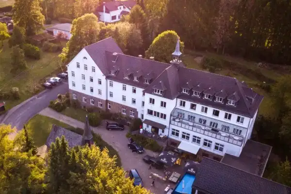Luftaufnahme des Klosters Ommerborn mit seinem markanten Turm, umgeben von Bäumen und einem Poolbereich.