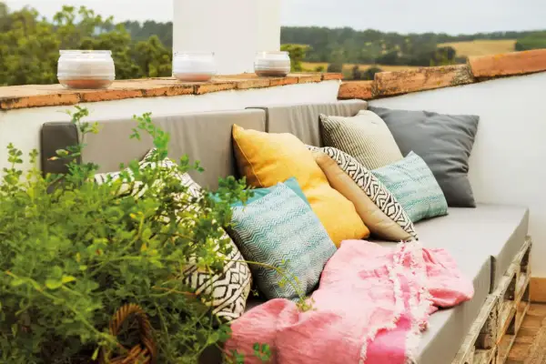 Sofá de palets con cojines coloridos y manta rosa, perfecto para una decoración chill out interiores. Velas aromáticas en la barandilla.