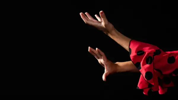 Manos expresivas de una bailaora de flamenco español, con un vestido rojo de lunares negros.