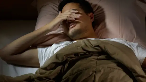 Man in bed, hand over eyes, can't sleep after long run. The runner's mind races, body tired but brain won't switch off.