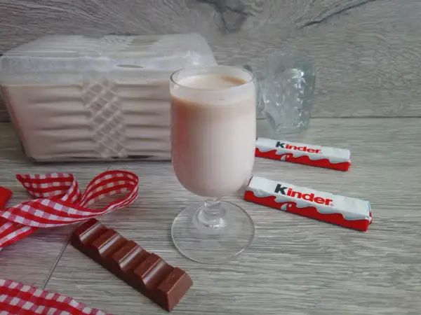 Pyszny likier z kinder czekoladek w kieliszku, obok batoniki i kawałek czekolady.