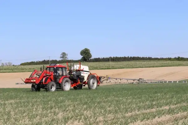 Czerwony traktor z opryskiwaczem polowym pracuje na polu. Tabela mieszania oprysków pomaga rolnikowi w precyzyjnym zabiegu.