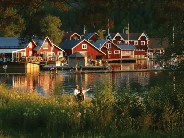 Solnedgång över Norrfjällsviken med röda sjöbodar och folk som njuter av kvällen vid vattnet.