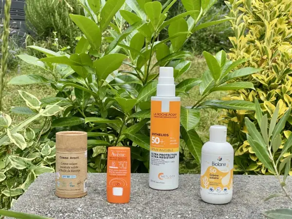 Quatre produits solaires, dont une crème solaire sans octocrylene, sont présentés sur un muret, entourés de verdure.