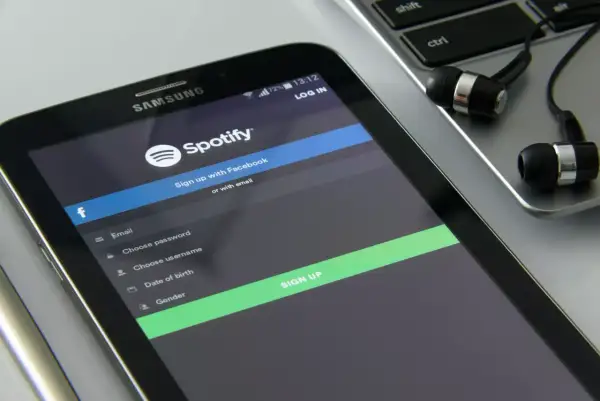 Ekran telefonu z aplikacją Spotify, formularzem rejestracji i słuchawkami na klawiaturze.