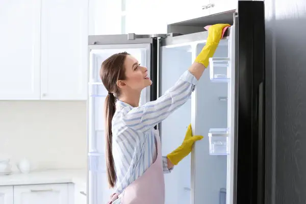 Donna con guanti gialli usa uno sgrassatore per pulire il frigo, rendendolo splendente.