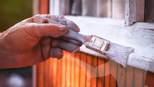 Main d'un peintre avec de la peinture blanche sur les doigts, tenant un pinceau. Astuces pour savoir comment enlever de la peinture sur les mains après le bricolage.