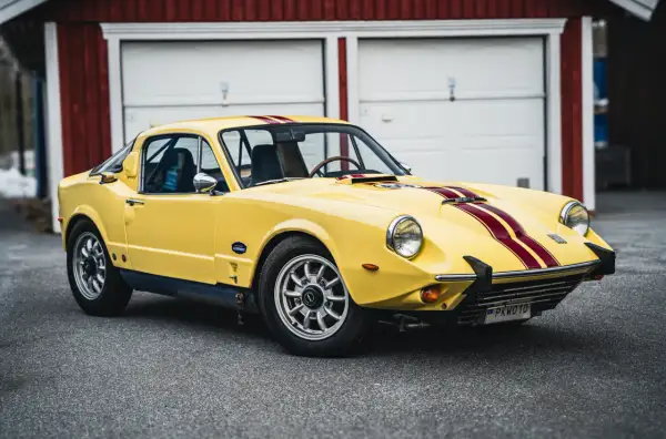 Gul Saab Sonett 2 med röda ränder, parkerad framför ett rött garage.