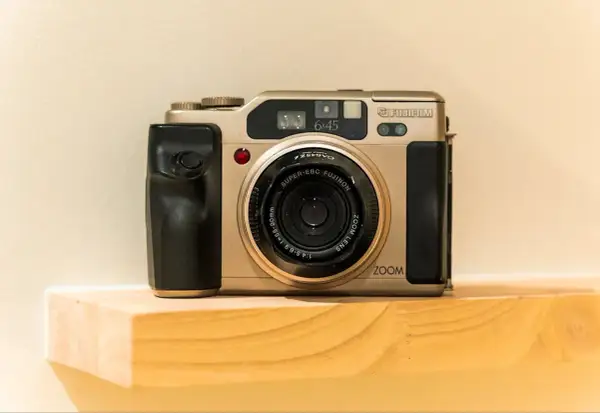 A gold Fujifilm 645 camera with a black grip sits on a wooden shelf.