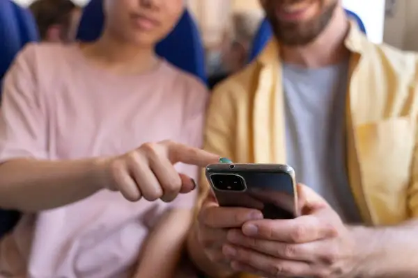 Pareja joven en un avión, compartiendo un teléfono. Quizás discutiendo sobre sus **relaciones parasociales** con influencers o celebridades.