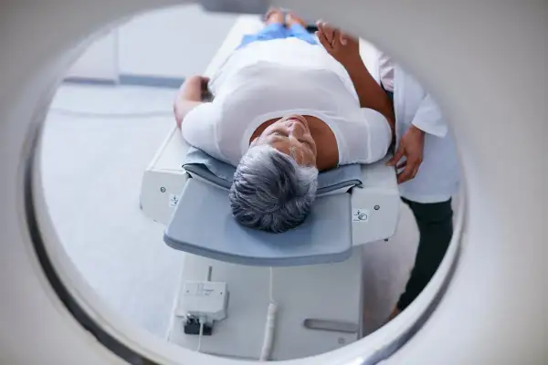 Une femme âgée se repose sur une table d'examen, prête pour un examen PET scan. C'est quoi un PET scan ? Une technique d'imagerie médicale.