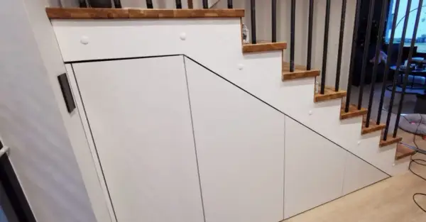 Pomysły na pojemne szafy: zabudowa przestrzeni pod schodami z białymi frontami i drewnianymi stopniami.