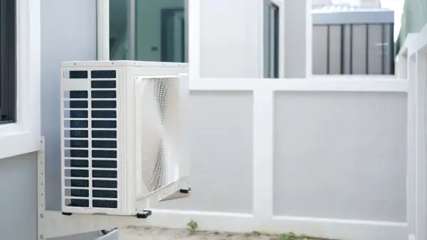 Unité extérieure d'une pompe à chaleur appartement, fixée sur un mur blanc. L'appareil est blanc avec des grilles bleues et un ventilateur visible.